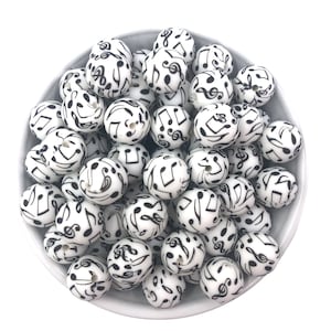May include: A bowl filled with white silicone beads with black musical notes printed on them.