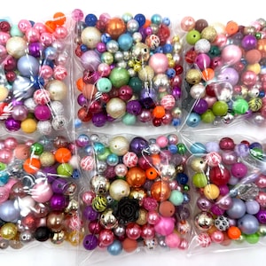 May include: Assortment of colorful plastic beads in various shapes and sizes, packaged in clear plastic bags. The beads are a mix of solid colors, patterns, and textures.