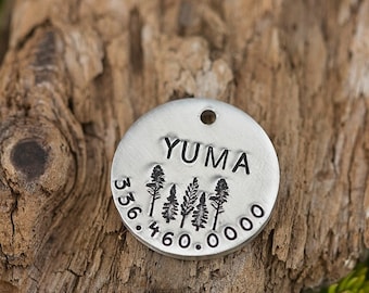 May include: Silver round tag with the word "YUMA" and a design of four trees. The tag also has the numbers "356.460.0000" engraved on it.