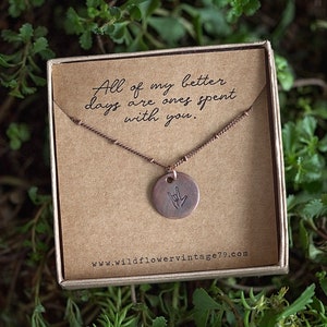 May include: A copper necklace with a round pendant featuring the American Sign Language symbol for "I love you". The necklace is in a brown box with the text "All of my better days are ones spent with you." and the website address "www.wildflowervintage79.com".