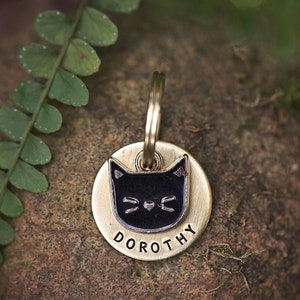 Op de afbeelding: Een ronde, gouden dierenpenning met een zwart katten silhouet en de naam "DOROTHY" erop gegraveerd.