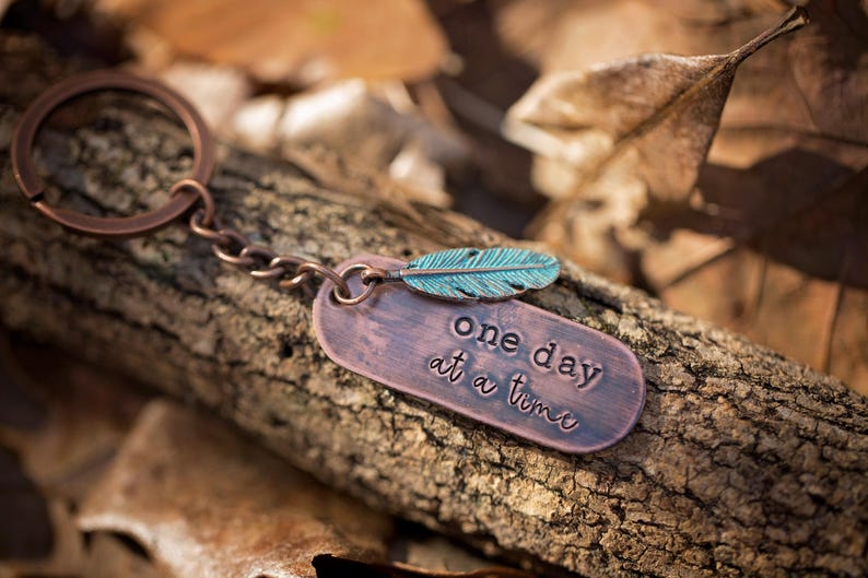 May include: A copper keychain with a feather charm and a tag that reads "one day at a time".