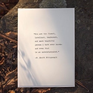 May include: A white card with a black typewriter font quote by F. Scott Fitzgerald. The quote reads, "You are the finest, loveliest, tenderest, and most beautiful person I have ever known- and even that is an understatement."
