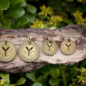 May include: Four brass charms with the New York City Transit Authority logo, featuring a stylized "Y" and the words "New York City Transit Authority". The charms are different sizes and are arranged on a piece of wood.