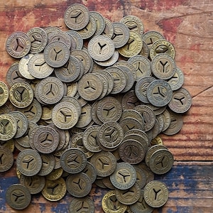 May include: A pile of vintage brass tokens with the words "Good For One Fare" and a stylized Y on a wooden surface.