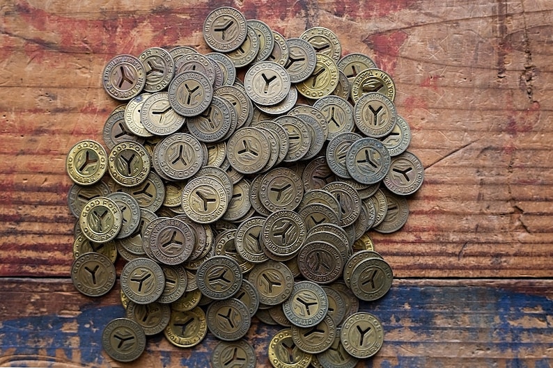 May include: A pile of vintage brass tokens with the words "Good For One Fare" and a stylized Y on a wooden surface.