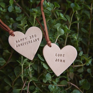 May include: Two brown leather heart-shaped tags with brown leather strings. The first tag says "Happy 3rd Anniversary". The second tag says "Love John".