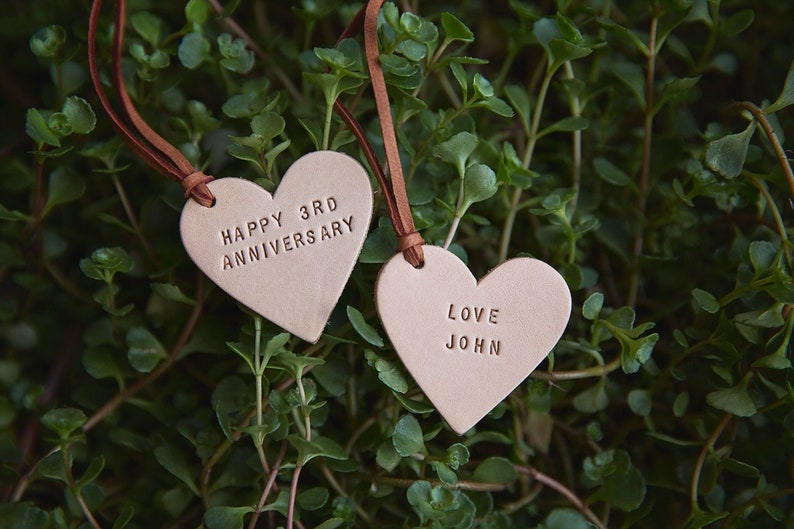 May include: Two brown leather heart-shaped tags with brown leather strings. The first tag says "Happy 3rd Anniversary". The second tag says "Love John".