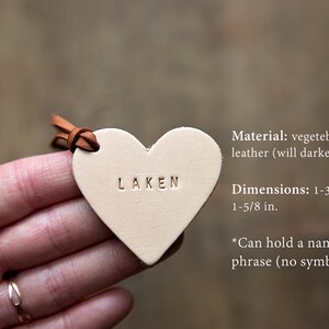 May include: A small, heart-shaped leather tag with the word "LAKEN" embossed on it. The tag is made of vegetable tanned leather and measures 1-3/4 inches by 1-5/8 inches. It can hold a name or short phrase.