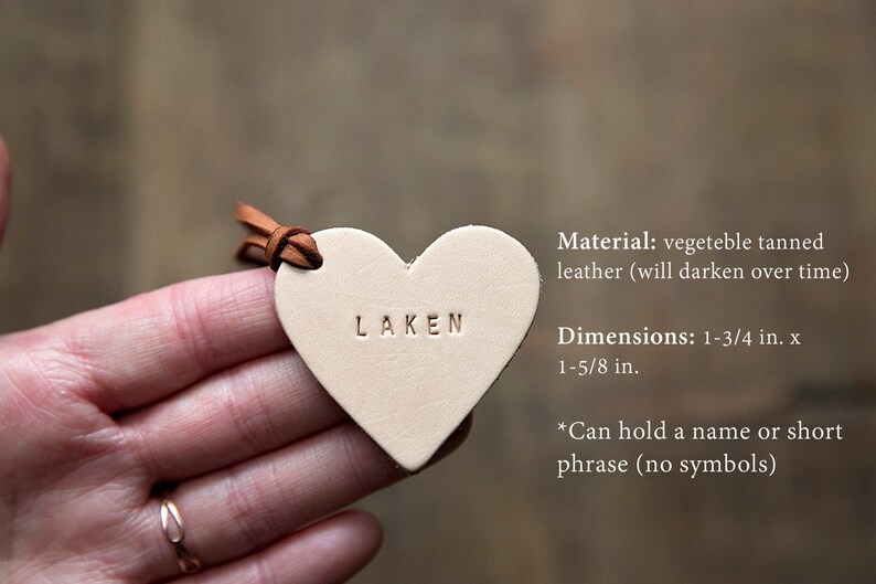 May include: A small, heart-shaped leather tag with the word "LAKEN" embossed on it. The tag is made of vegetable tanned leather and measures 1-3/4 inches by 1-5/8 inches. It can hold a name or short phrase.