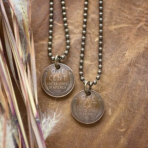 May include: Two gold chain necklaces with a copper penny pendant on each. The pennies are dated 1943 and 1944 and read "One Cent, United States of America".