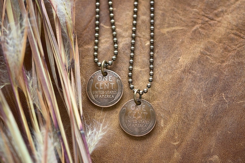 May include: Two gold chain necklaces with a copper penny pendant on each. The pennies are dated 1943 and 1944 and read "One Cent, United States of America".