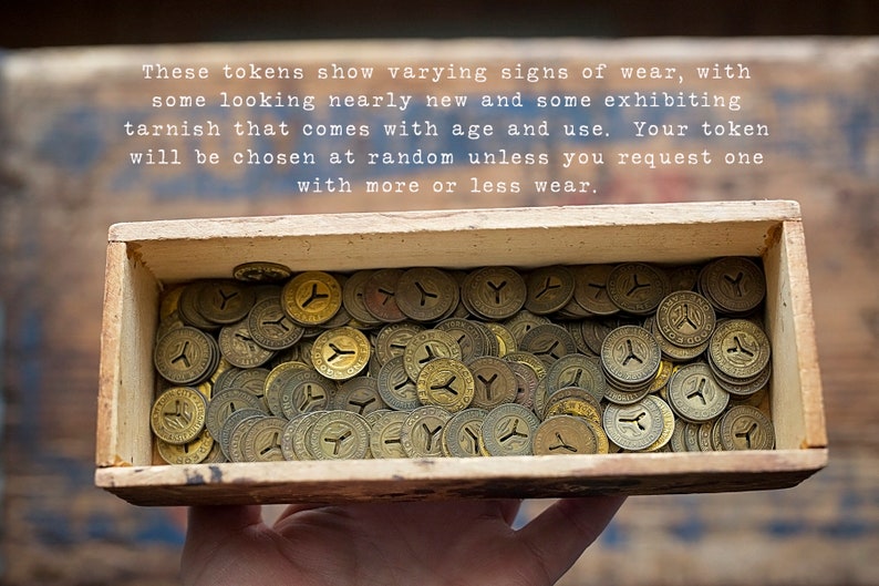 May include: A wooden box filled with a large quantity of brass tokens. The tokens are all circular and have a Y-shaped design in the center. The tokens show varying signs of wear, with some looking nearly new and some exhibiting tarnish that comes with age and use.