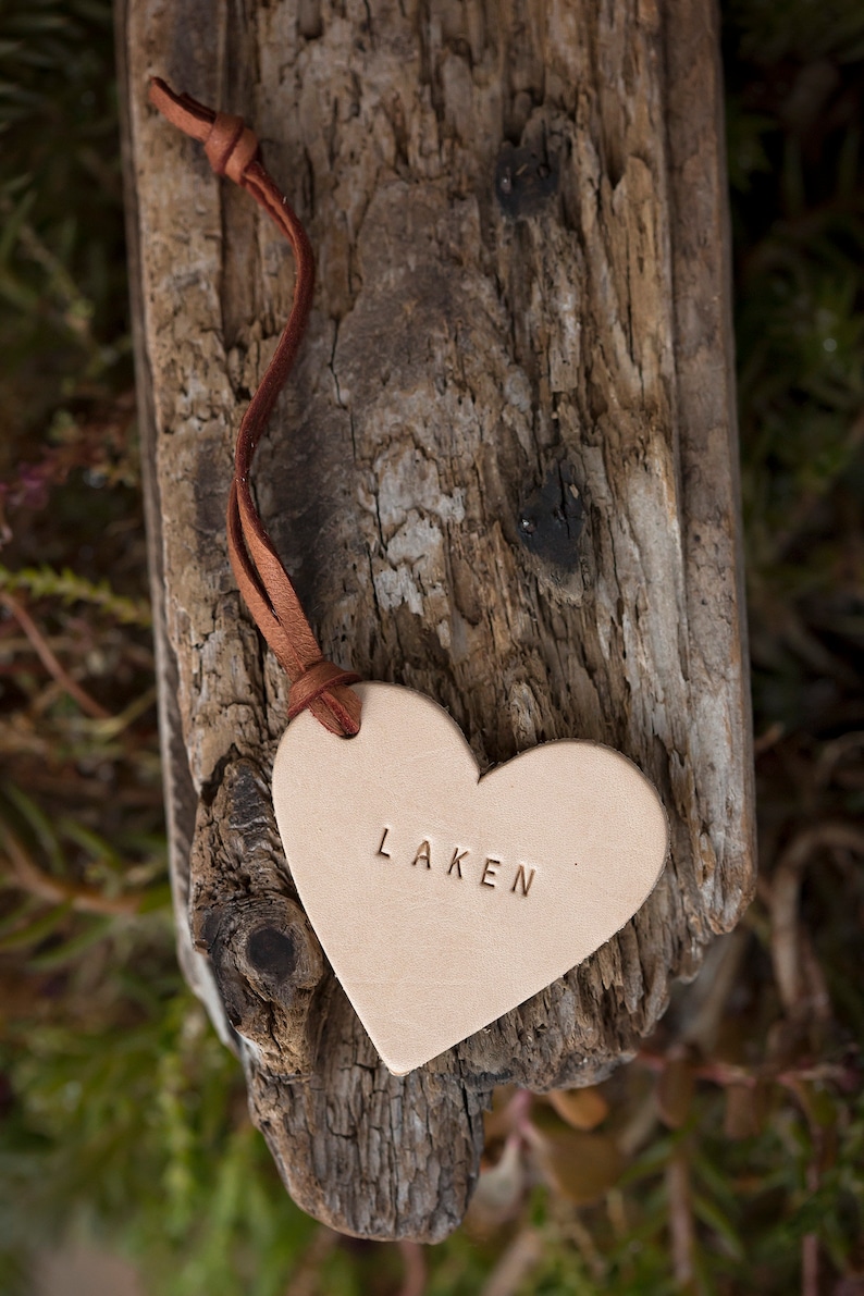 May include: A light brown leather heart-shaped tag with a brown leather cord. The tag has the word "LAKEN" embossed on it.