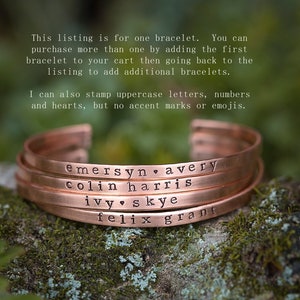 May include: Copper-colored bracelets with stamped names and a heart symbol. The bracelets are stacked on top of each other. The text on the bracelets includes names like "emersyn avery" and "colin harris".