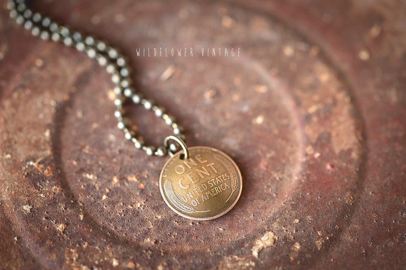 May include: A gold-toned necklace with a vintage one-cent coin pendant. The coin features the words "ONE CENT" and "UNITED STATES OF AMERICA".