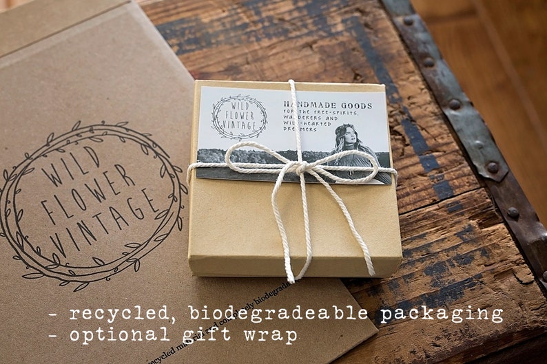 May include: A small, tan gift box tied with white twine, featuring a label with the text "HANDMADE GOODS" and "WILD FLOWER VINTAGE." The box is on a rustic wooden surface, with a larger cardboard box in the background.