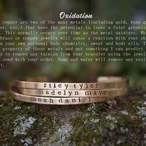 May include: Three gold-colored metal bracelets stacked on top of each other, each engraved with a name. The top bracelet reads "riley tyler", the middle one "madelyn maye", and the bottom one "noah daniel". The bracelets are displayed on a mossy surface.