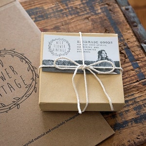 Pu&ograve; includere: Una piccola scatola di cartone marrone legata con uno spago. La scatola ha un'etichetta che recita "Handmade Goods for the Tree-Spirits, Wild-Hearted Dreamers". La scatola &egrave; appoggiata su una superficie di legno.