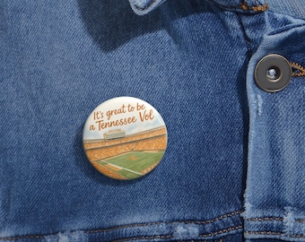 Könnte beinhalten: Ein runder Button mit dem Text "It's great to be a Tennessee Vol" und einer Stadionillustration. Der Button hat einen weißen Hintergrund mit orangefarbenen, grünen und braunen Details. Er ist an einer blauen Jeansjacke befestigt.
