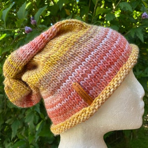 May include: A hand-knitted beanie in shades of yellow, orange, and pink with a brown leather tag that reads "Stacey's Knitwits Australia".