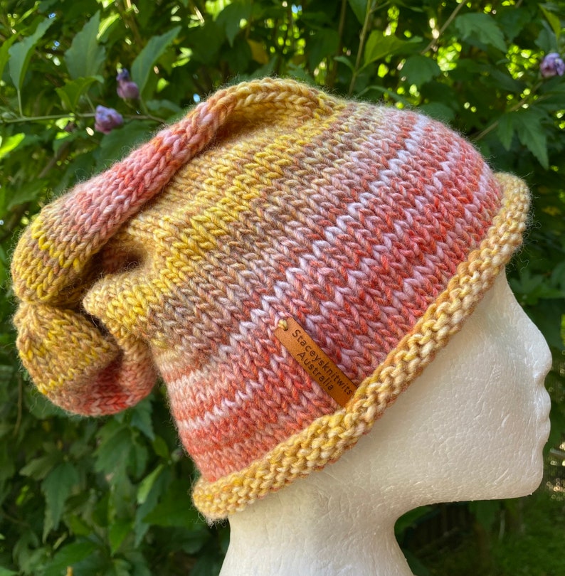 May include: A hand-knitted beanie in shades of yellow, orange, and pink with a brown leather tag that reads "Stacey's Knitwits Australia".