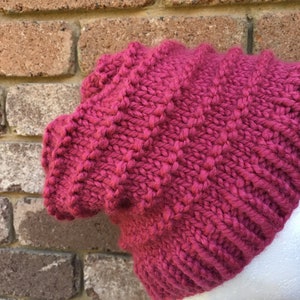 Pode incluir: Um gorro de malha rosa com um padr&atilde;o texturizado. O gorro est&aacute; em uma cabe&ccedil;a de manequim branca.