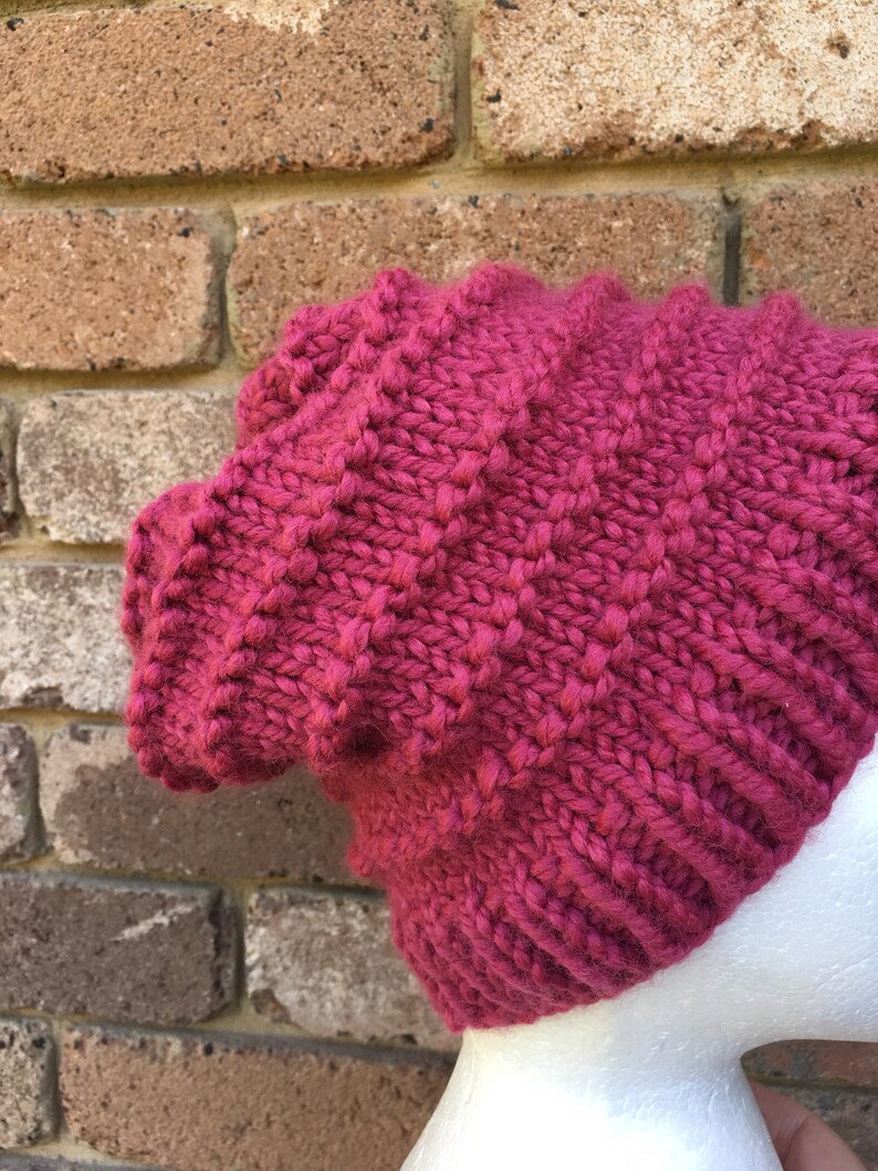 Pode incluir: Um gorro de malha rosa com um padr&atilde;o texturizado. O gorro est&aacute; em uma cabe&ccedil;a de manequim branca.