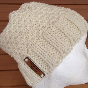May include: A white knitted beanie with a brown leather label that reads "Stacey Knit Wits, Australia".