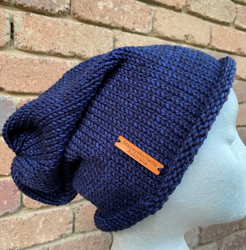 May include: A dark blue knitted beanie with a slouchy fit. The beanie has a brown leather tag with the text "Stacey's Knits Australia".