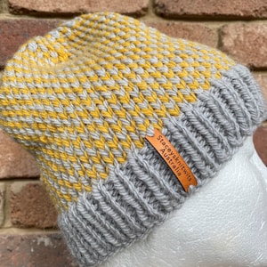 May include: A gray and yellow knitted beanie with a brown leather tag that reads "Stacey's Knits Australia".