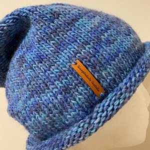 May include: Blue and teal knitted beanie with a brown leather tag that reads "SleepyKnitter's Australia".
