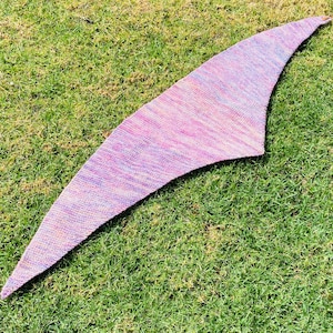 May include: A triangular knitted shawl featuring a variegated color palette of soft pink, lavender, and subtle orange hues. The textile displays a consistent garter stitch pattern throughout, with a tapered shape that extends to pointed ends.