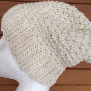 May include: A white knitted beanie hat with a slouchy fit. The hat is made of a soft, textured yarn.