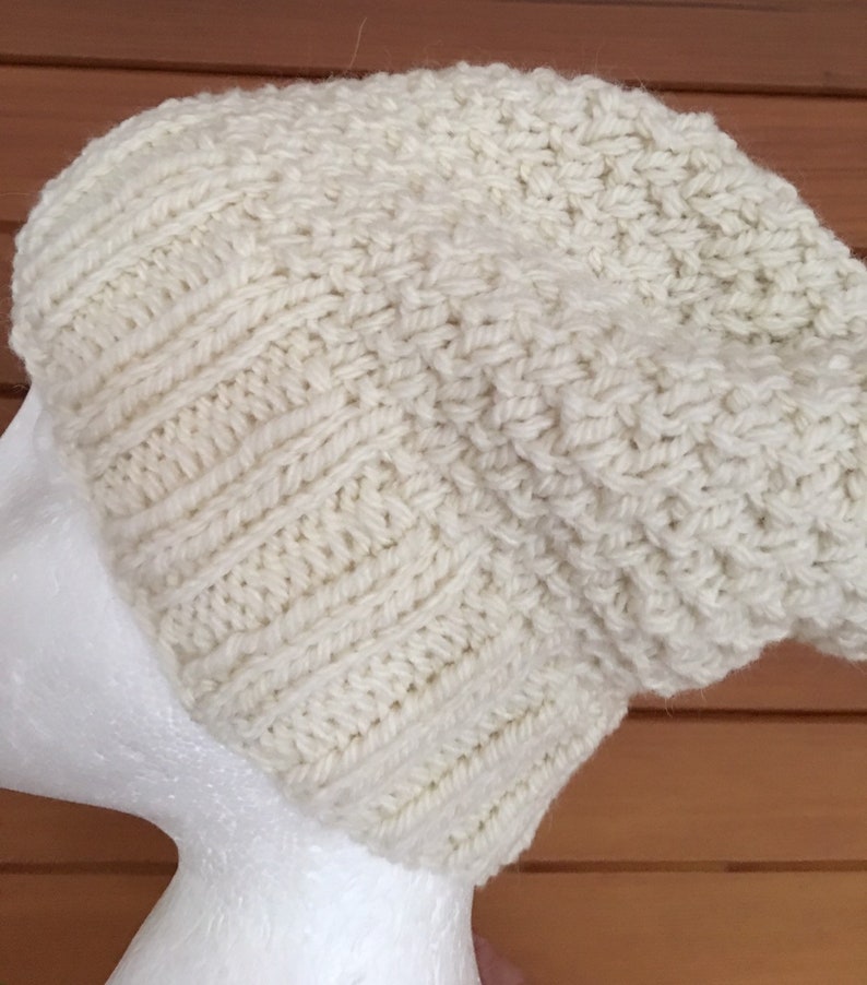 May include: A white knitted beanie hat with a slouchy fit. The hat is made of a soft, textured yarn.