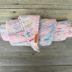 May include: A hand-knitted scarf featuring a variegated yarn pattern with soft pastel pink, blue, yellow, and white flecks. The scarf is folded in a layered arrangement and includes a small, rectangular brown leather tag labeled StaceyKnits Australia.