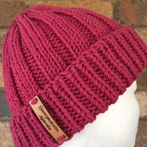 May include: A pink knitted beanie with a brown leather label that reads "Stacey's Knitwits, Australia".