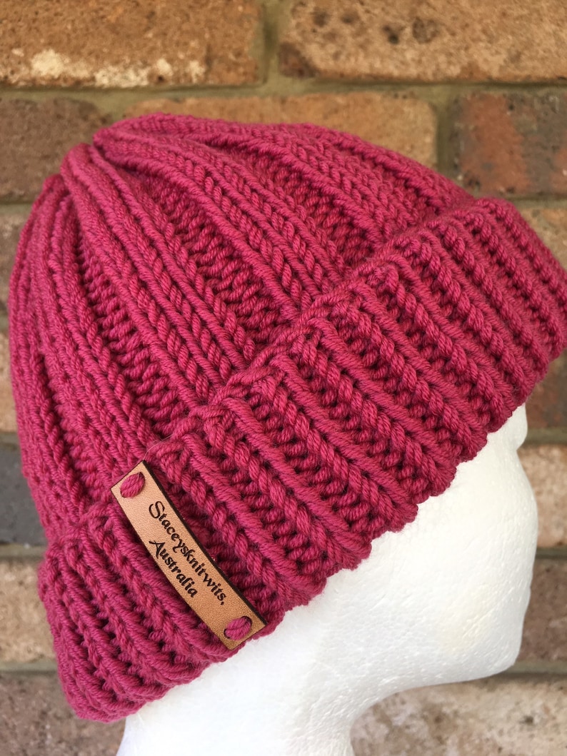 May include: A pink knitted beanie with a brown leather label that reads "Stacey's Knitwits, Australia".
