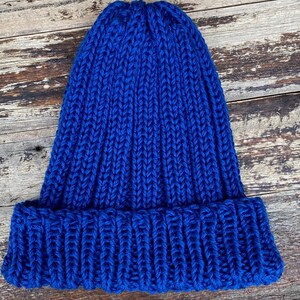 May include: A blue knitted beanie hat with a ribbed texture. The hat has a folded brim.