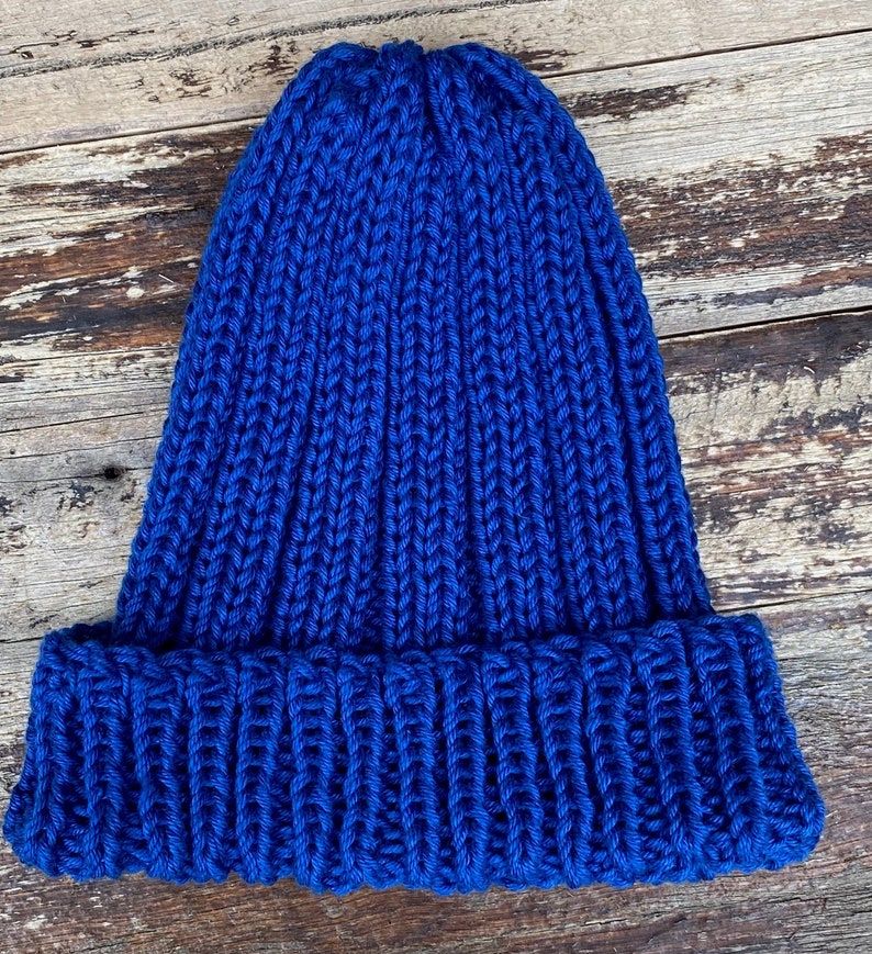 May include: A blue knitted beanie hat with a ribbed texture. The hat has a folded brim.
