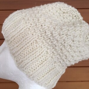 May include: A white knitted beanie hat with a textured stitch pattern. The hat is made of a soft, warm yarn and is perfect for cold weather.