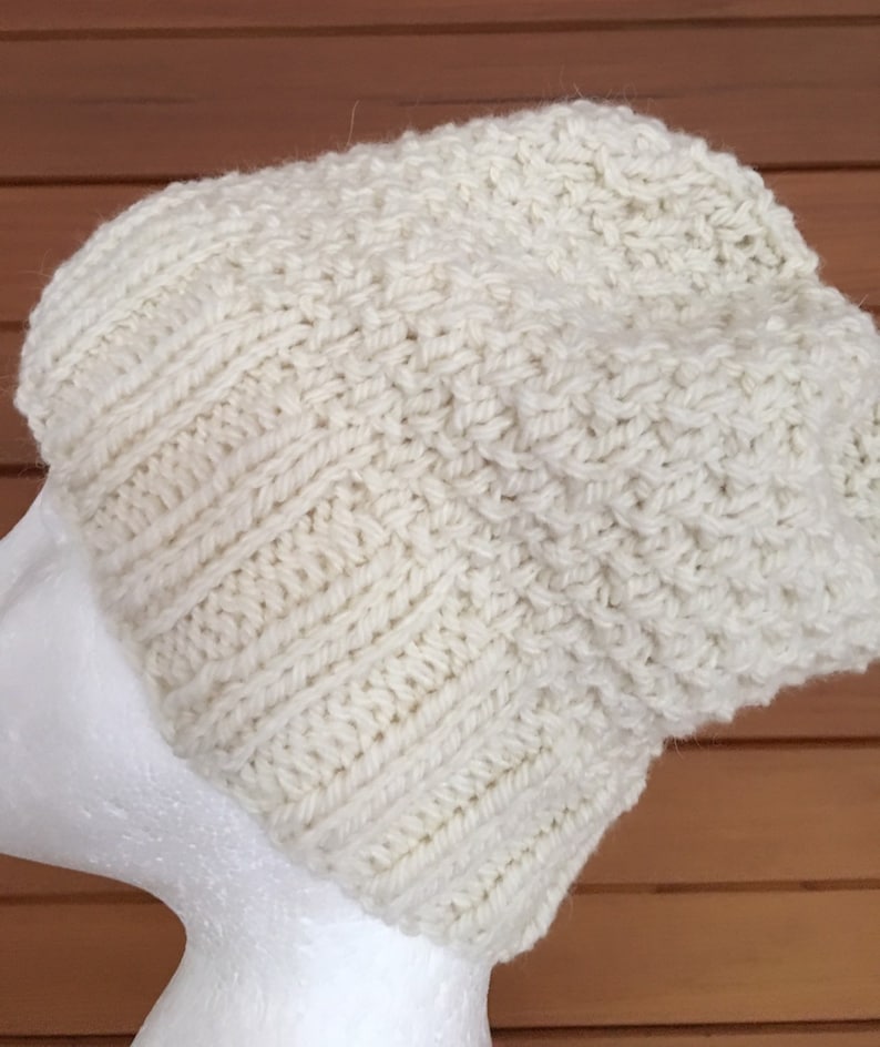 May include: A white knitted beanie hat with a textured stitch pattern. The hat is made of a soft, warm yarn and is perfect for cold weather.
