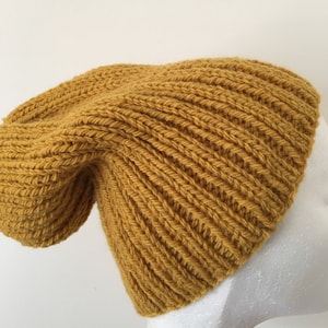 Peut inclure: Un bonnet en tricot jaune moutarde avec une texture côtelée.