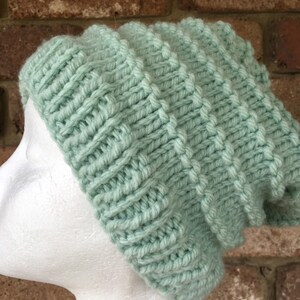 Pode incluir: Um gorro de malha de cor verde claro com um padr&atilde;o de ponto texturizado.