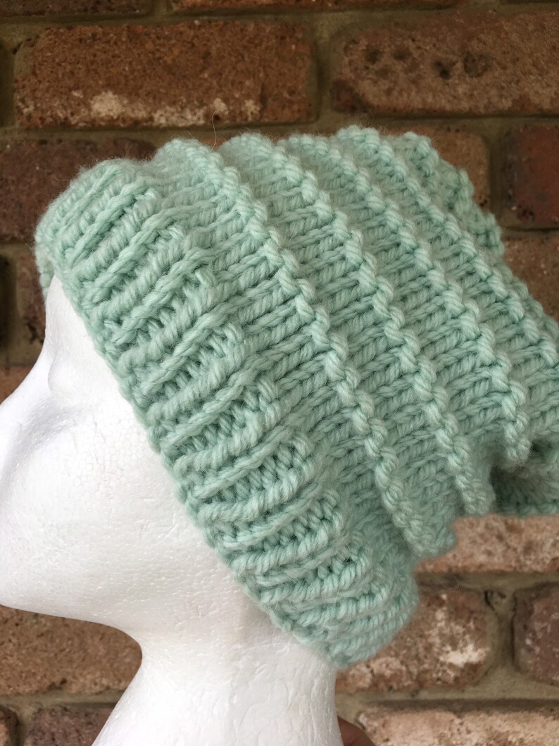 Pode incluir: Um gorro de malha de cor verde claro com um padr&atilde;o de ponto texturizado.