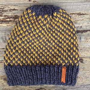 May include: A dark gray and yellow knitted beanie with a brown leather tag that reads "Staceyknits Australia".