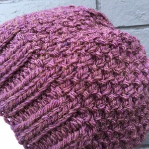 May include: A purple knitted beanie hat with a textured stitch pattern.