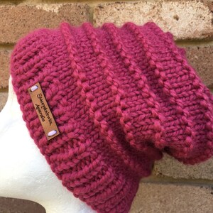 Pode incluir: Um gorro de malha rosa com uma etiqueta de couro marrom que diz "SleepyKnitWits, Austr&aacute;lia".