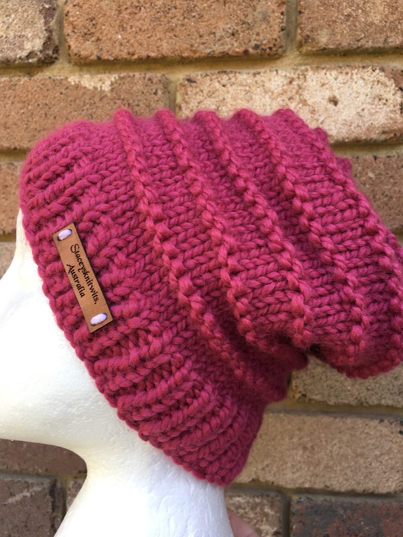 Pode incluir: Um gorro de malha rosa com uma etiqueta de couro marrom que diz "SleepyKnitWits, Austr&aacute;lia".