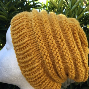 May include: A mustard yellow knitted beanie hat with a slouchy fit. The hat is made with a thick yarn and has a ribbed texture.